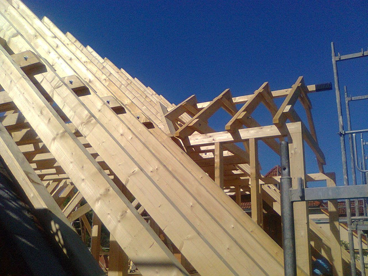 Die hölzerne Dachkonstruktion entsteht vor einem klaren blauen Himmel.