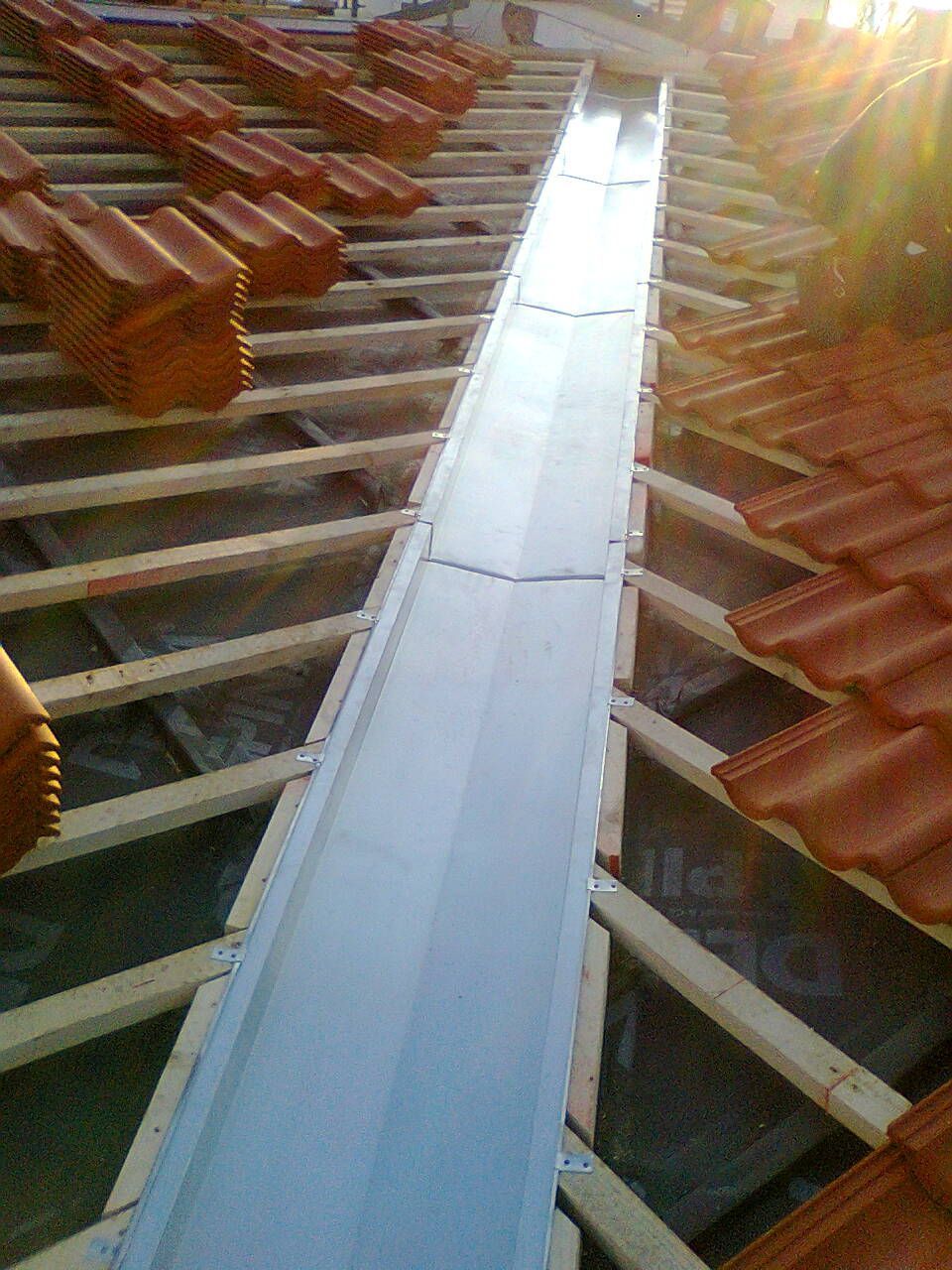 Montage einer Kehlblechabdeckung aus Metall auf einem Ziegeldach. Holzbalken und orangefarbene Ziegel sind sichtbar.