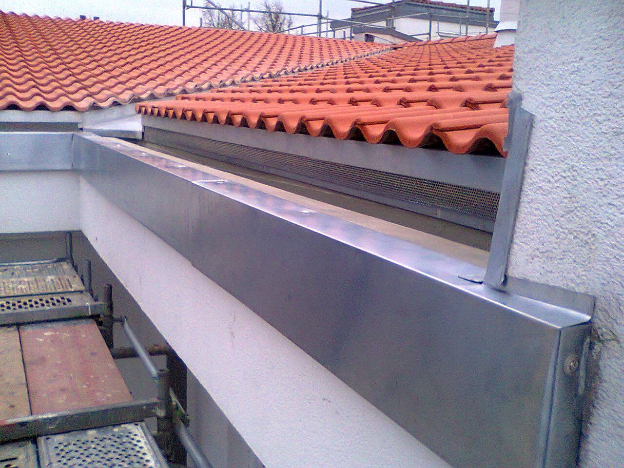 Eine Metallrinne wurde entlang der Dachlinie eines mit roten Ziegeln gedeckten Daches und einer weißen Wand installiert.
