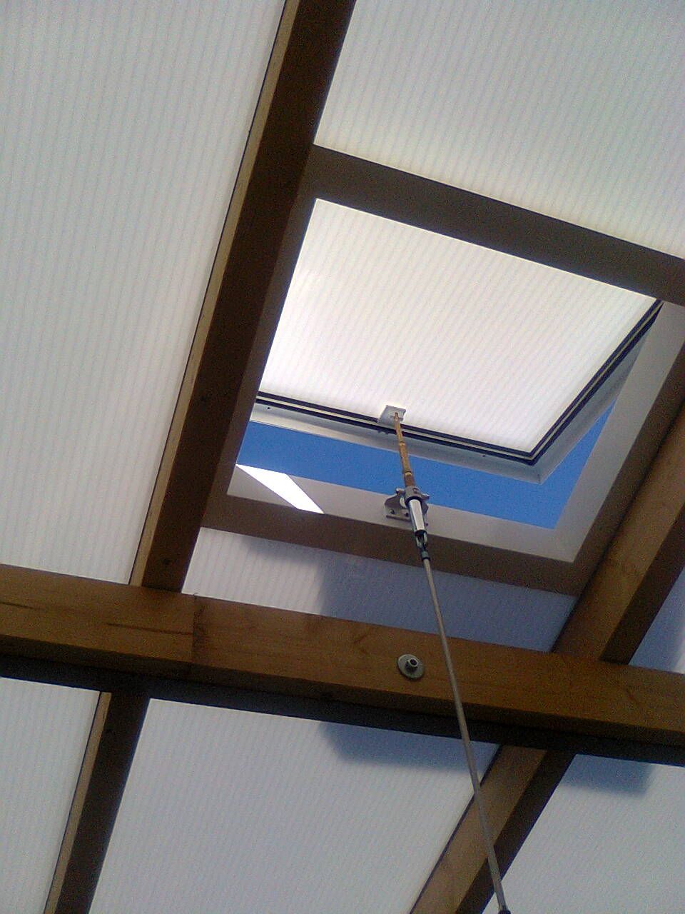 Oberlicht in einem Holzfachwerkdach; offen zum blauen Himmel; eine lange Stange dient zum Öffnen und Schließen.