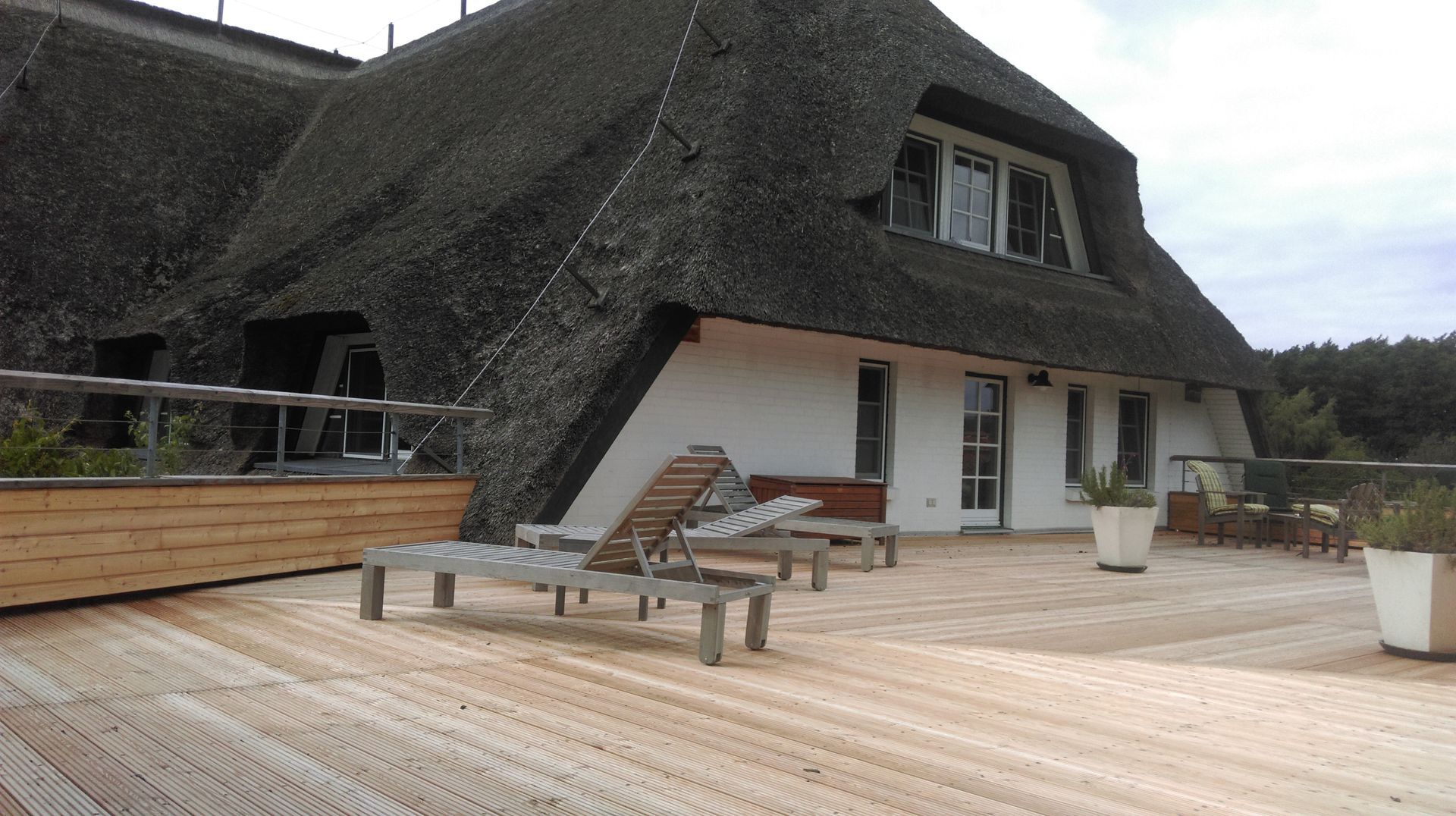 Ein Gebäude mit Reetdach und einer Holzterrasse mit Liegestühlen.