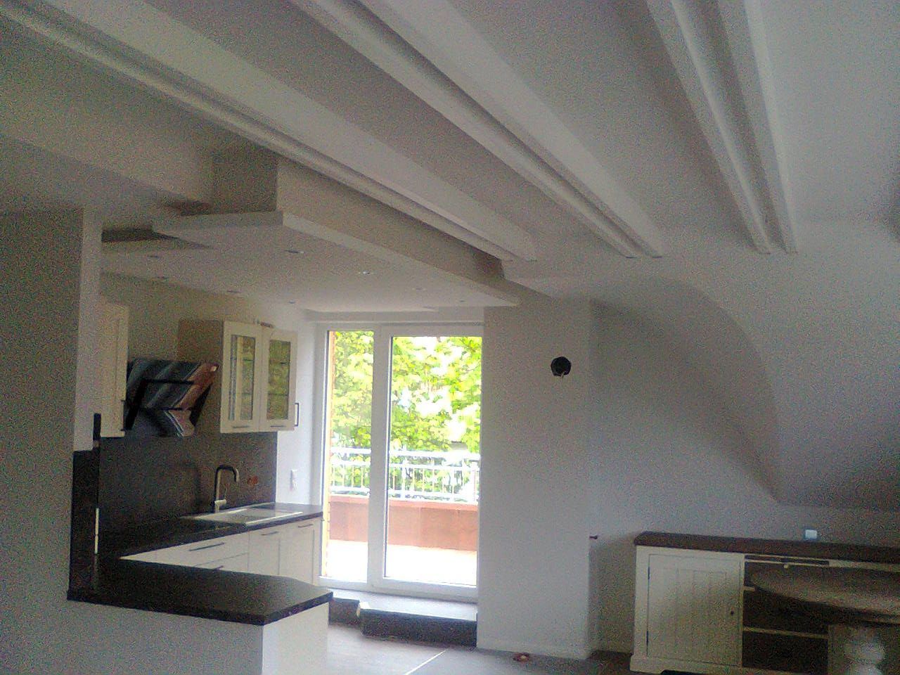 Innenansicht eines Zimmers mit Küche und Balkon, zu sehen sind eine weiße Decke, weiße Wände und weiße Schränke.