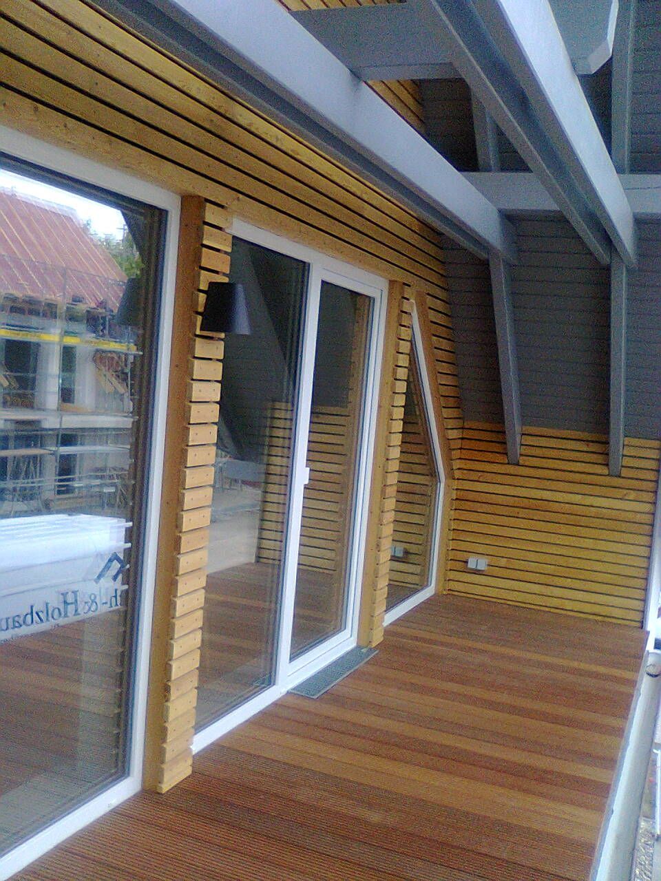 Außenansicht eines Gebäudes mit Holzverkleidung, einer Terrasse und Glasschiebetüren.