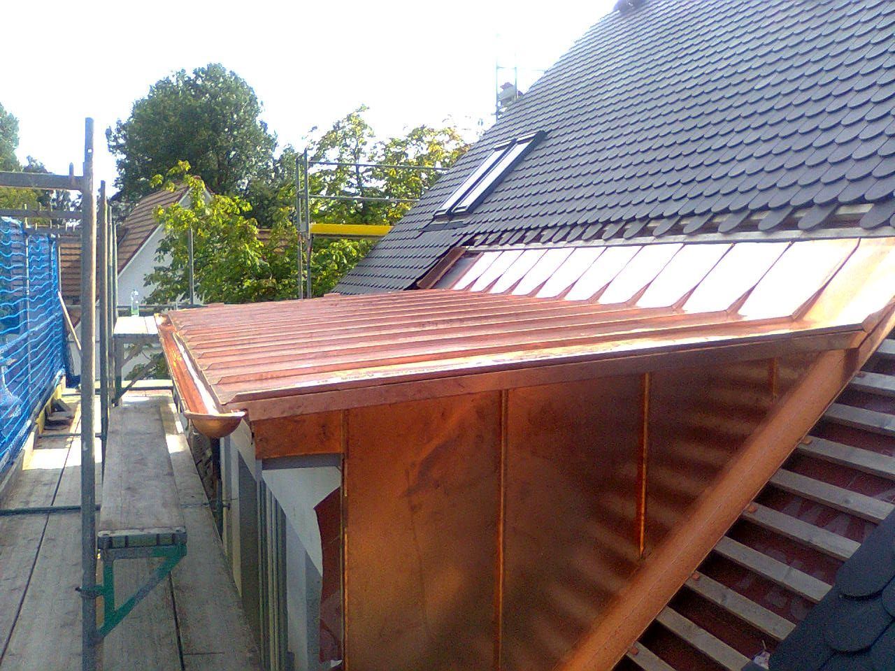Kupferverkleideter Dachaufsatz mit Dachrinne; angrenzend an ein dunkles Ziegeldach und ein Baugerüst.