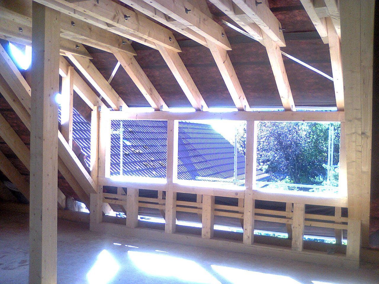 Innenansicht eines unfertigen Dachbodens mit Holzrahmen, Fensteröffnungen und einfallendem Sonnenlicht.