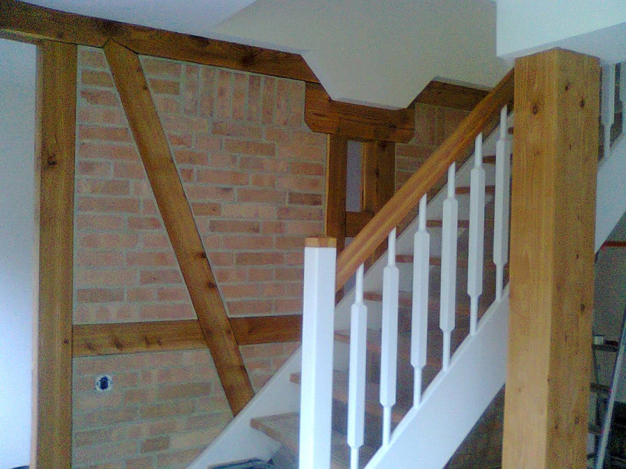 Treppe mit weißen Balustern und hölzernem Handlauf vor einer freiliegenden Ziegelwand und Holzbalken.