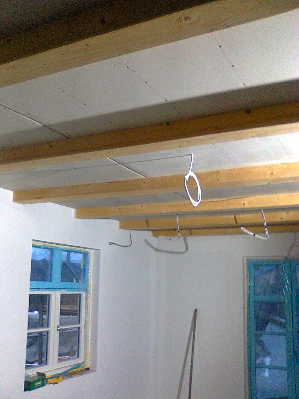 Innenansicht eines im Bau befindlichen Raumes mit Holzbalkendecke, zwei Fenstern und freiliegenden Leitungen.