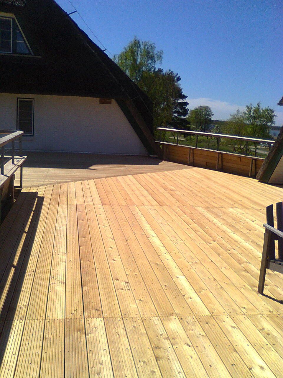 Holzterrasse an einem Gebäude, Geländer, sonniger Tag.
