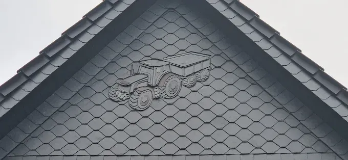 Graues Dach mit einem Flachrelief eines Traktors mit Anhänger.