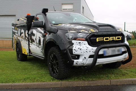 Un pick-up Ford Ranger modifié, avec une peinture noire et blanche, un tuba et un pare-buffle, est stationné sur l'herbe.