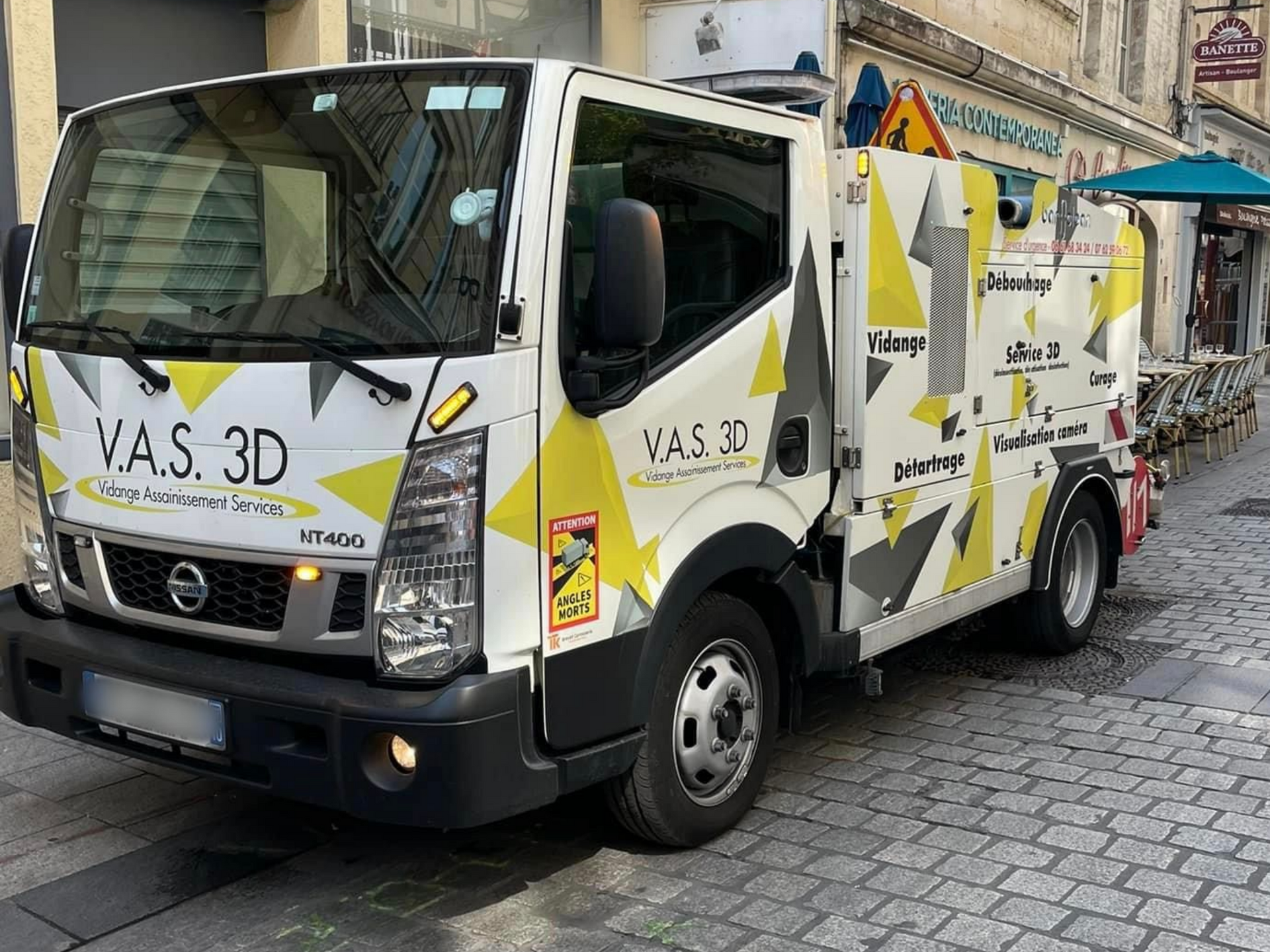 Camion de service blanc et jaune stationné dans une rue pavée.