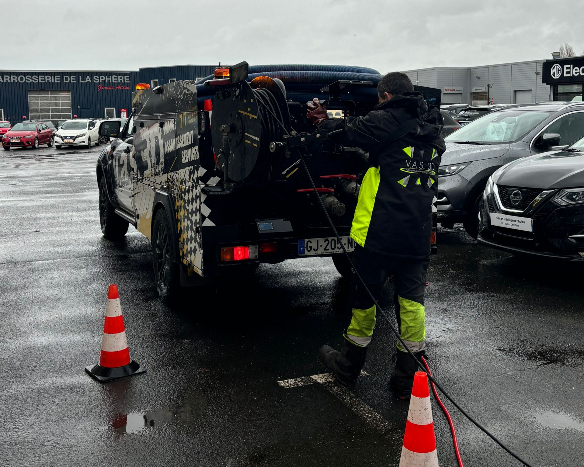 Un dépanneur se prépare à remorquer un véhicule sur un parking automobile par temps de pluie.