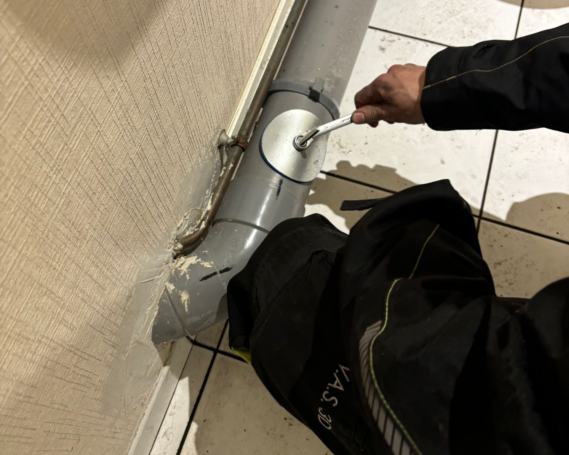 Une personne utilise une clé pour serrer un collier de serrage autour d'un tuyau gris près d'un mur.