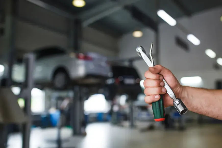 Mano sosteniendo una llave inglesa y un dado en un taller de reparación de automóviles con coches en elevadores.