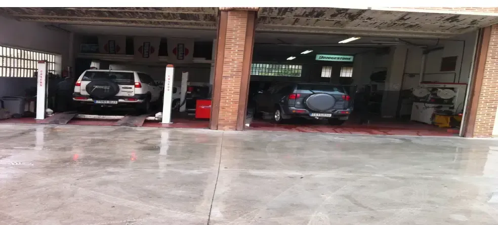 Dos mecánicos trabajan debajo de un coche en un taller. Uno lleva gafas de seguridad.