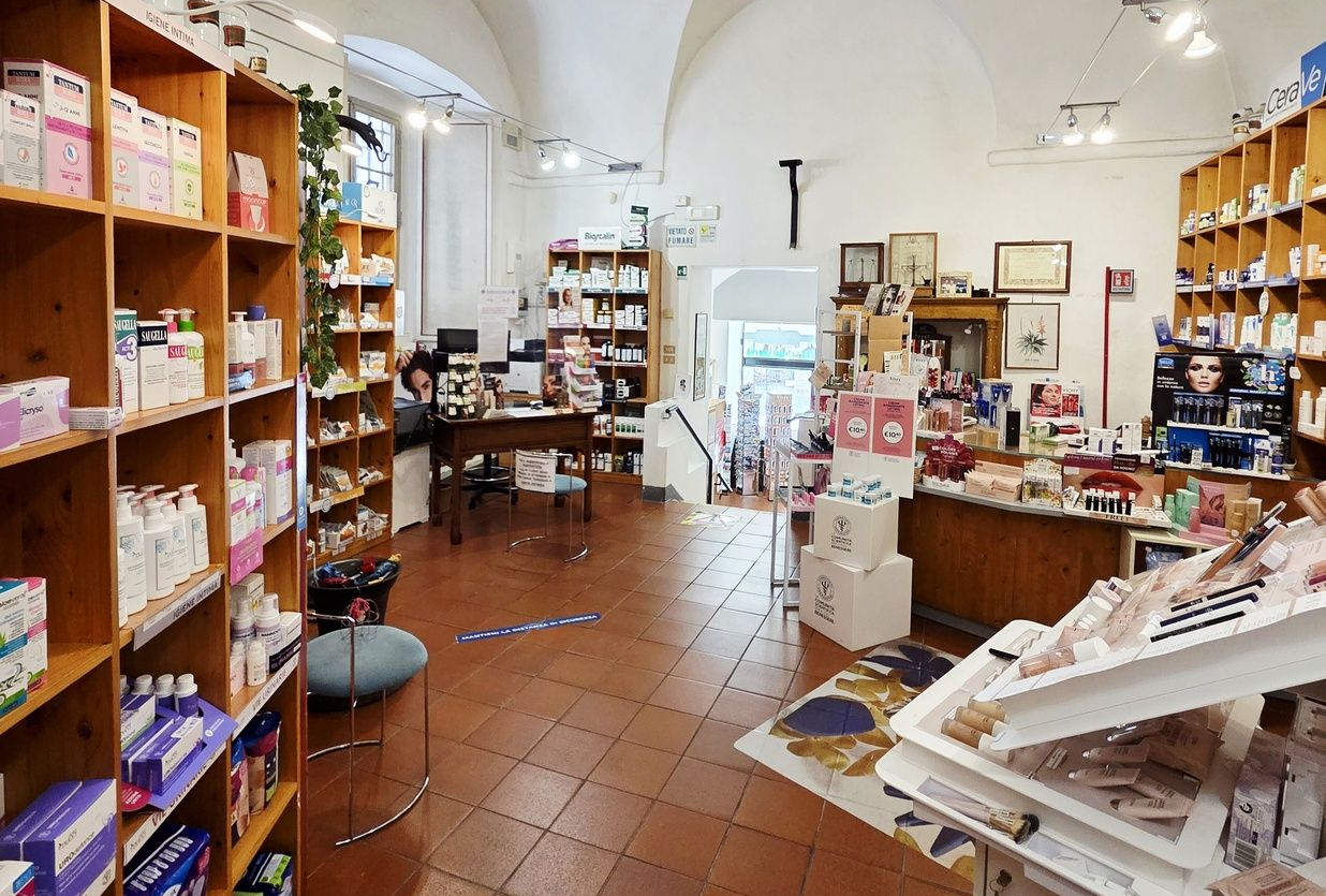 Luminoso interno di farmacia con scaffali in legno, pavimento piastrellato e banconi riforniti di prodotti per la salute.