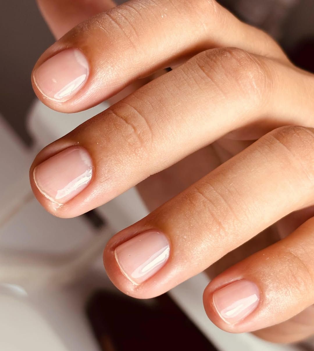 Primer plano de dedos cuidadosamente manicurados con uñas de color rosa pálido sobre un fondo desenfocado.