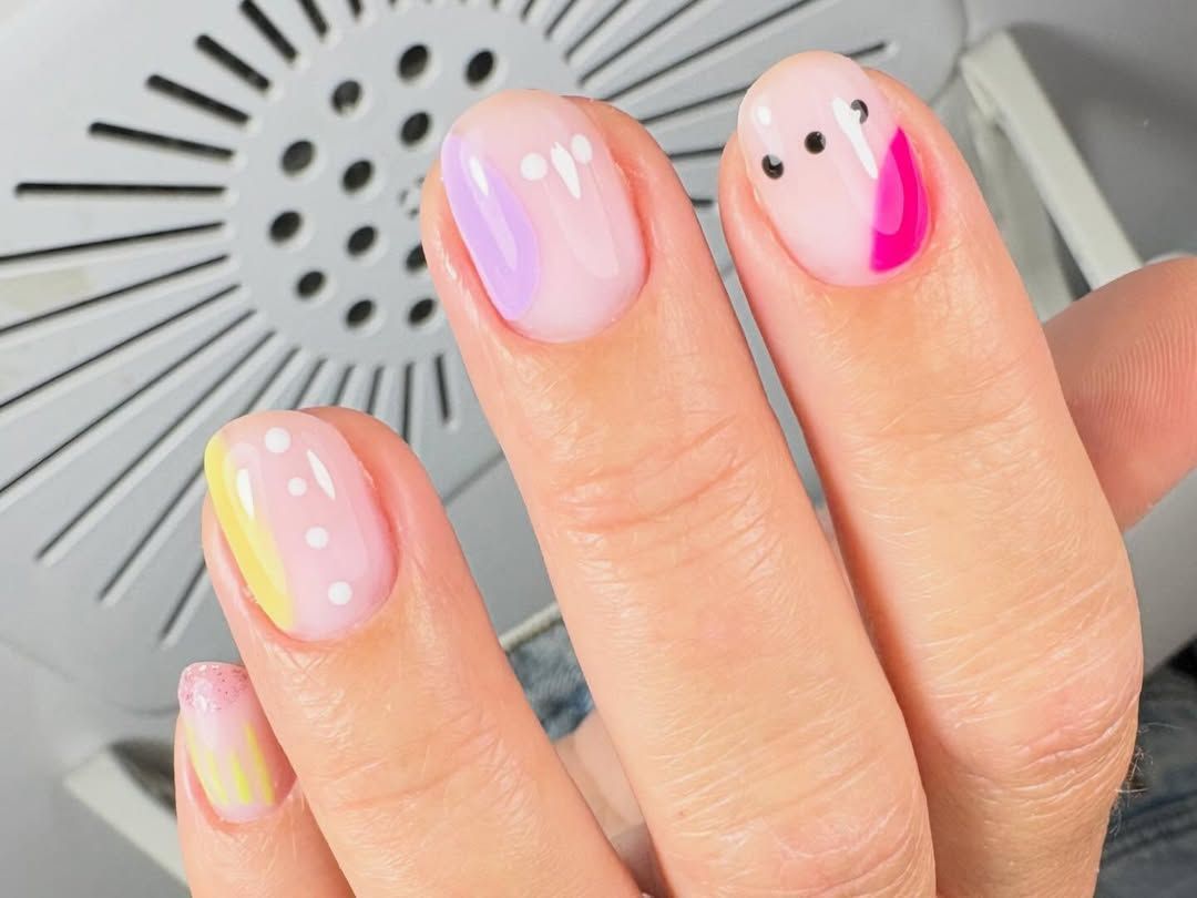 Primer plano de uñas manicuradas con esmalte rosa pastel y pequeños detalles de puntos negros en una mano.