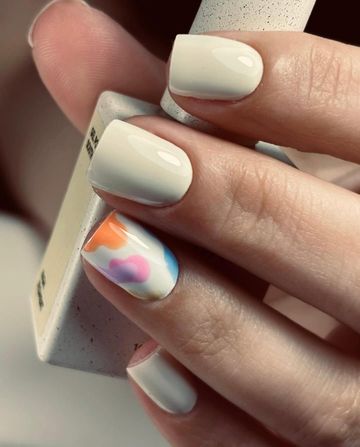 Primer plano de una mano con uñas blancas brillantes y una uña con un diseño abstracto en tonos pastel.