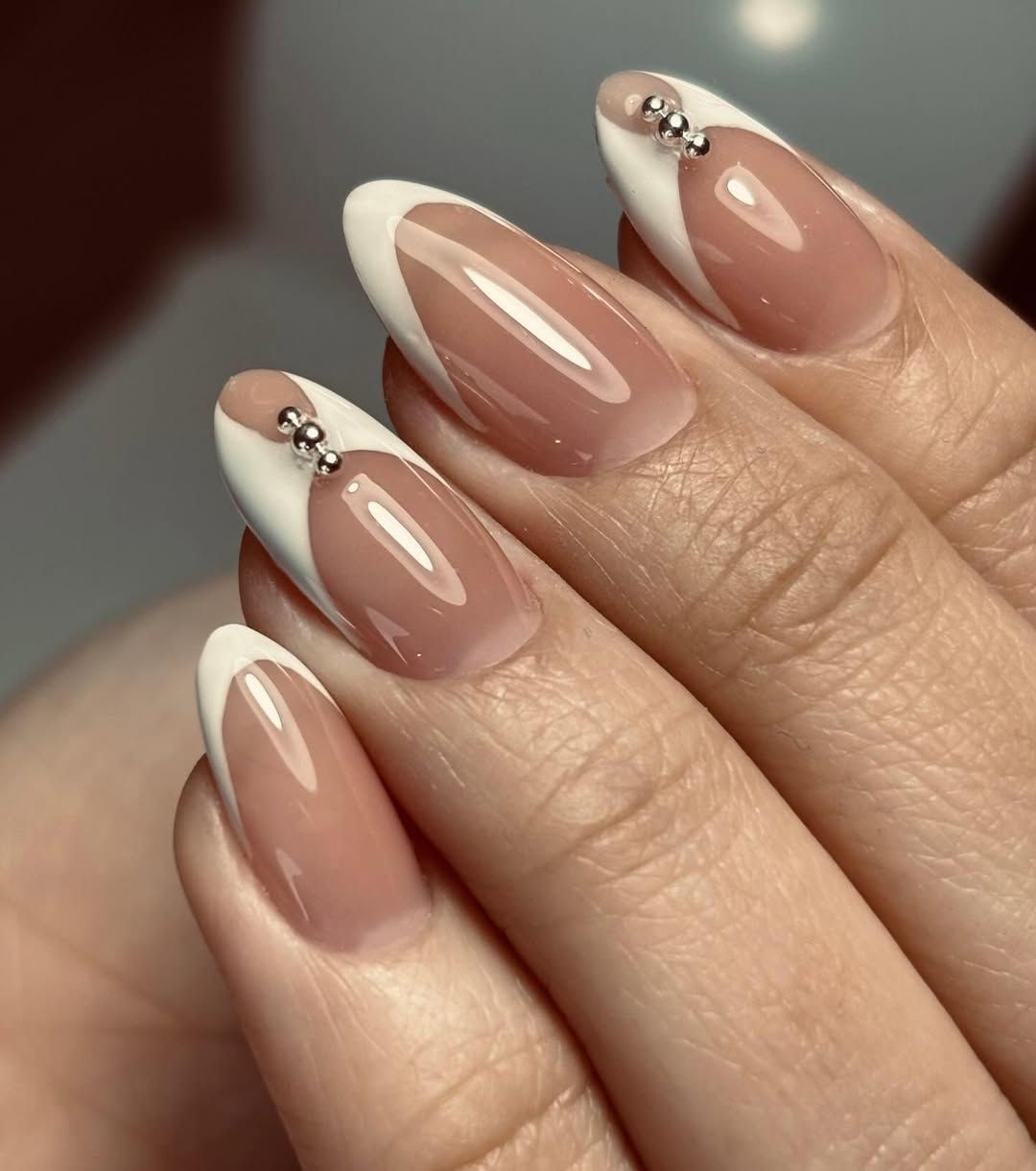 Primer plano de uñas con manicura francesa color nude, puntas blancas y pequeños adornos plateados.