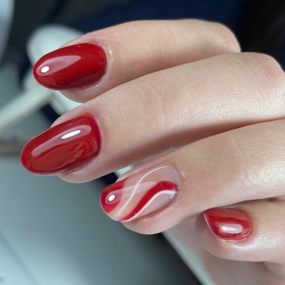Primer plano de una mano con uñas manicuradas brillantes de color rojo y blanco con remolinos.