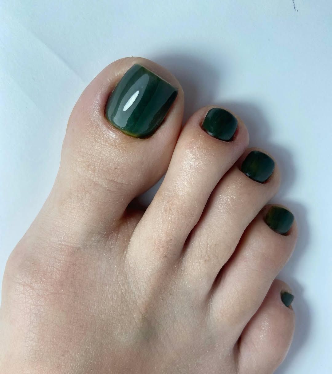 Dedos de los pies con esmalte de uñas verde oscuro sobre un fondo claro.