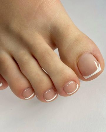 Primer plano de los dedos de los pies con pedicura francesa blanca sobre un fondo claro.