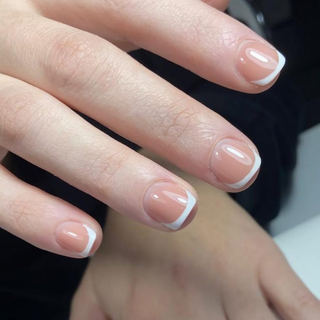 Primer plano de manos con uñas rosa nude y puntas francesas blancas.