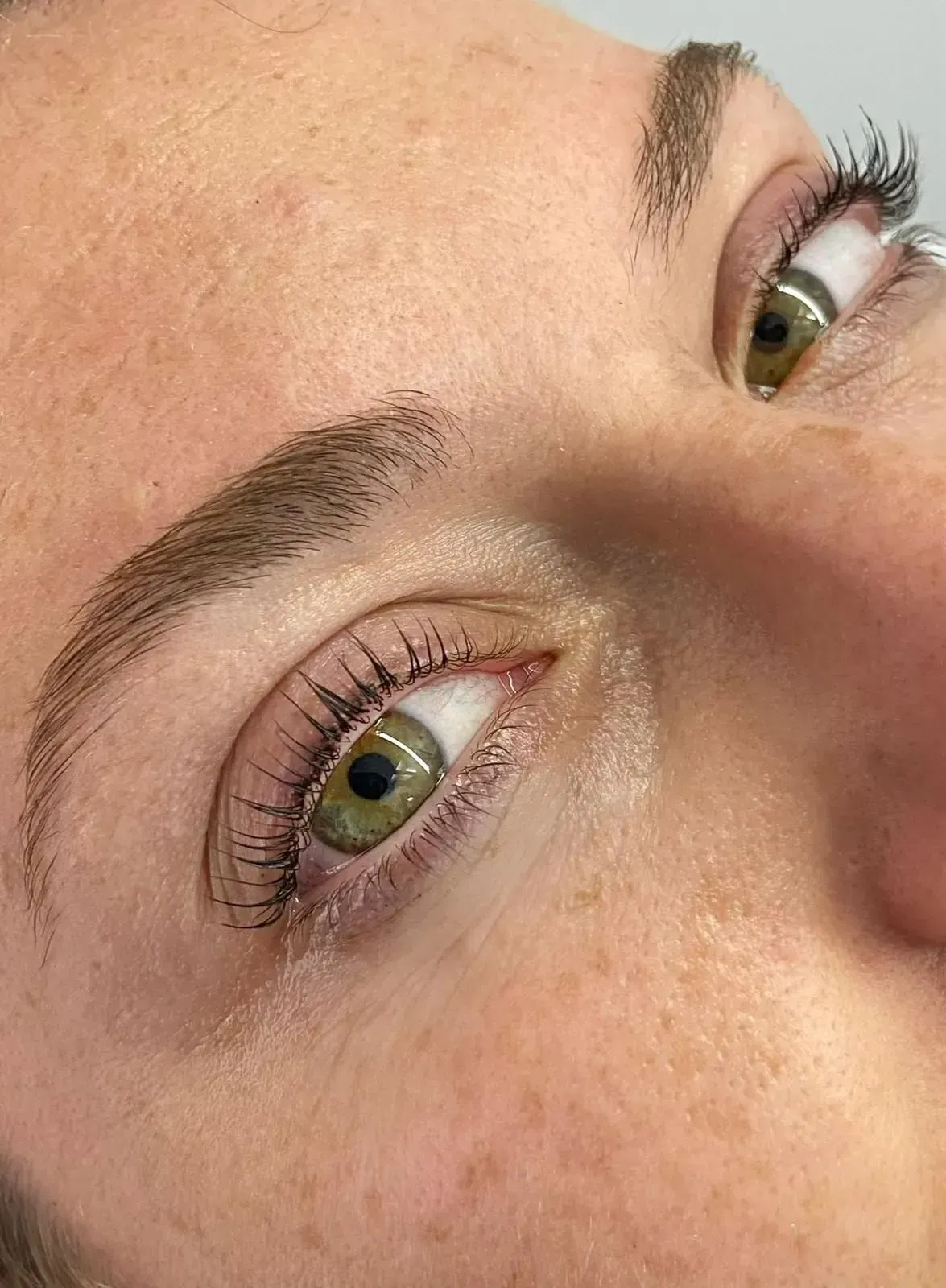 Primer plano de un rostro con ojos verdes, cejas verdes y textura de piel natural.