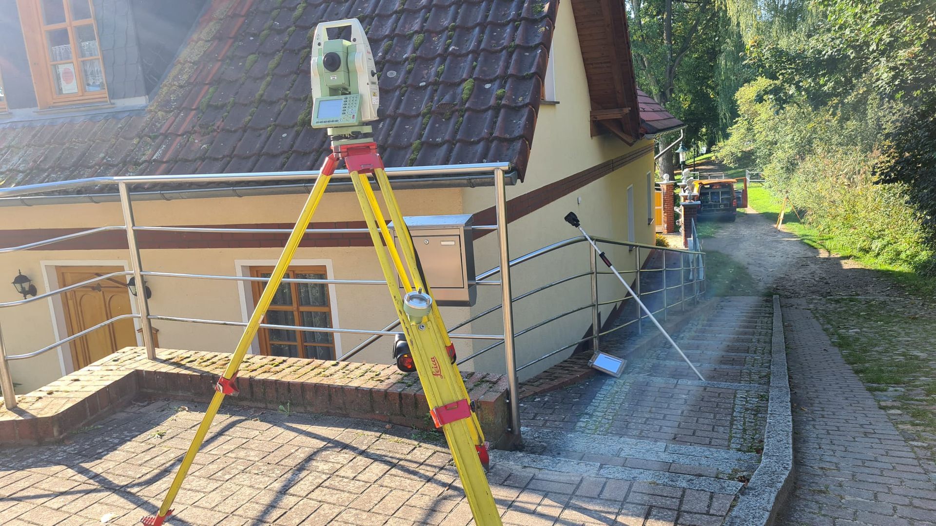 Vermessungsstativ mit Laser-Nivelliergerät neben einem Haus und Solarpaneele auf einer abschüssigen Einfahrt