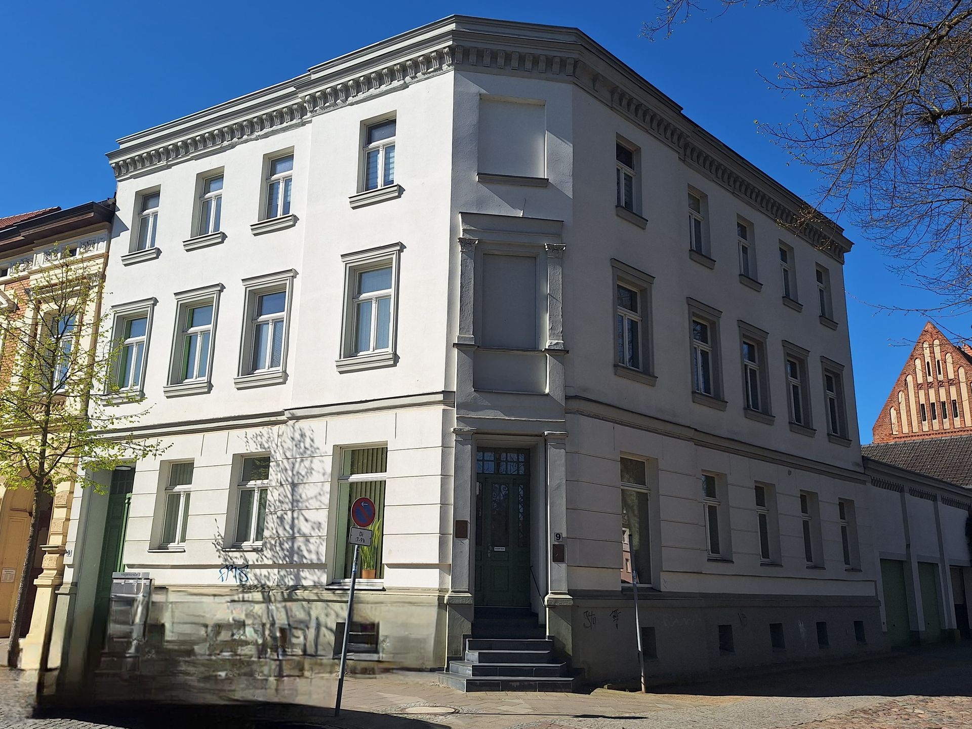 Weißes Eckreihenhaus mit verzierten Fenstern an einer sonnigen Straße unter blauem Himmel