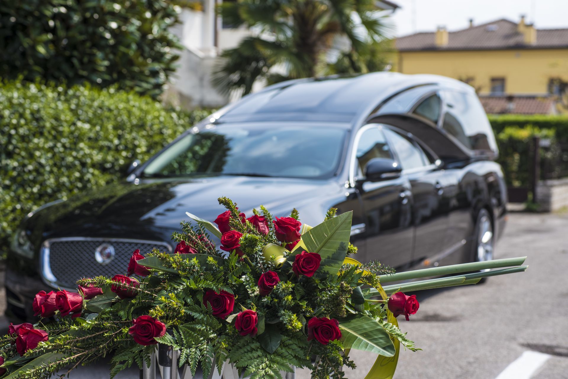 Corbillard noir orné de roses rouges dans un cimetière ou un lieu de funérailles.