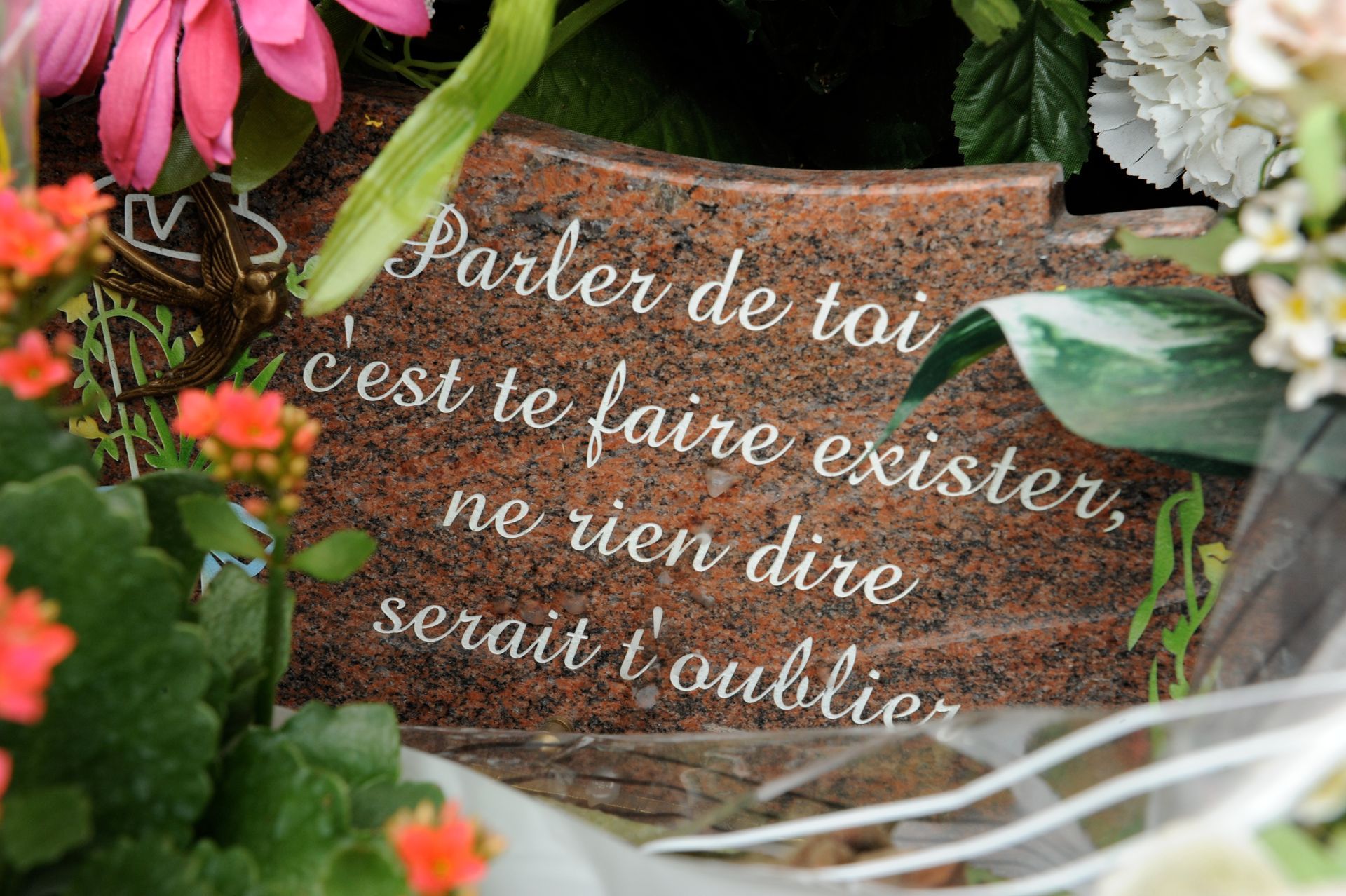 Citation française sur un panneau en marbre rustique entouré de fleurs et de verdure.