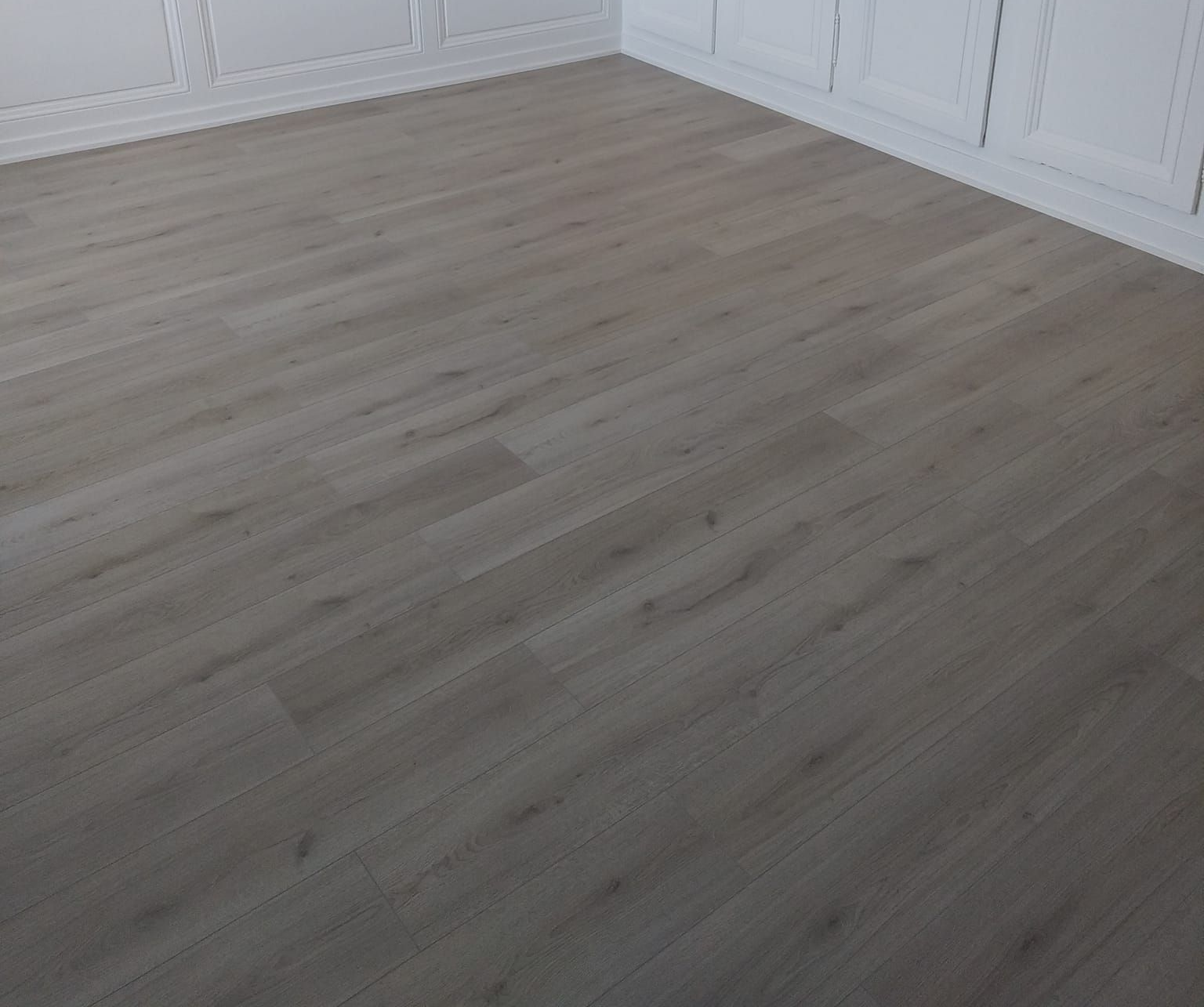 Chambre vide avec parquet gris clair et garnitures blanches.