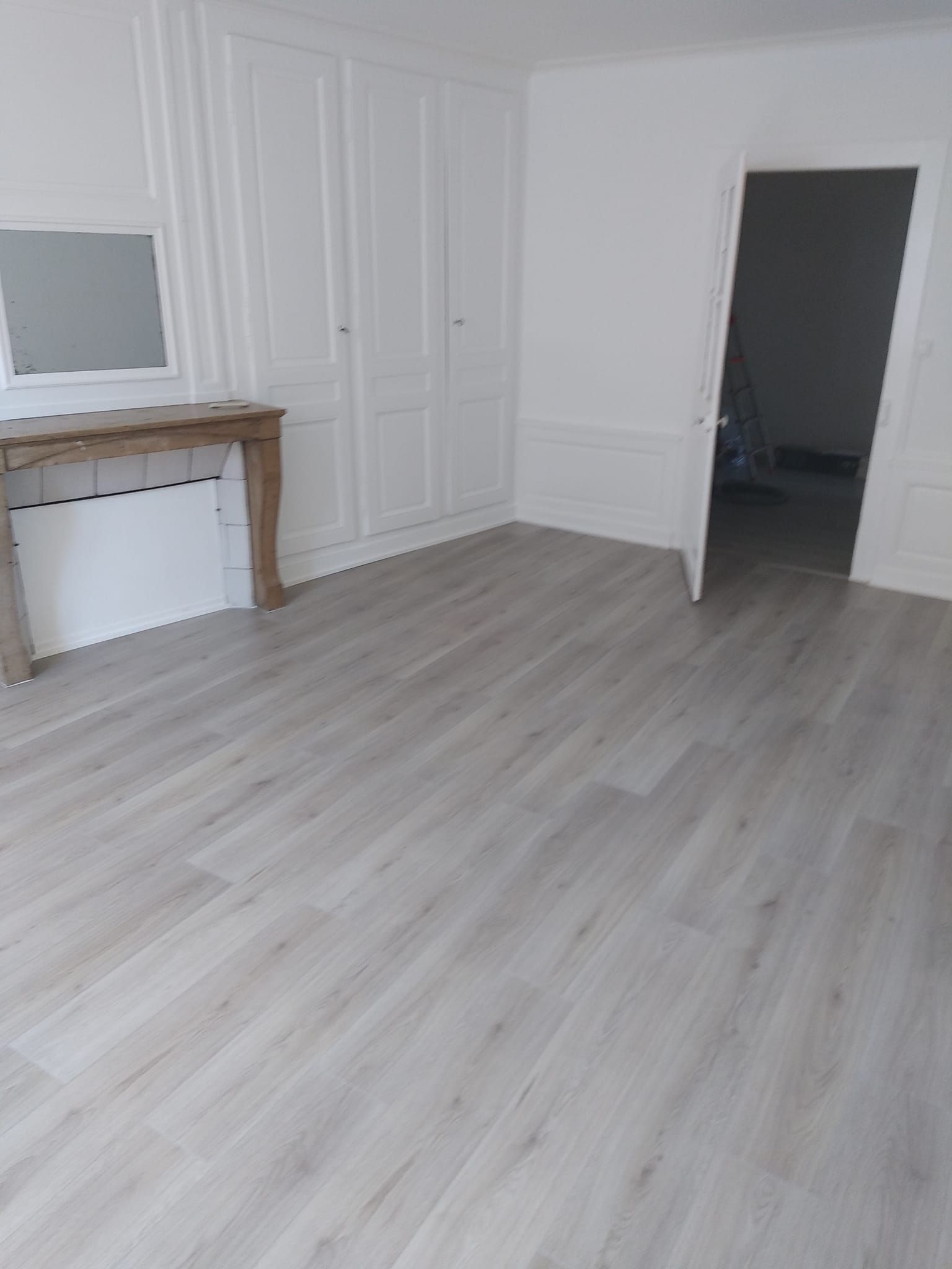Pièce vide avec parquet imitation bois clair, murs blancs et armoires encastrées, porte ouverte.