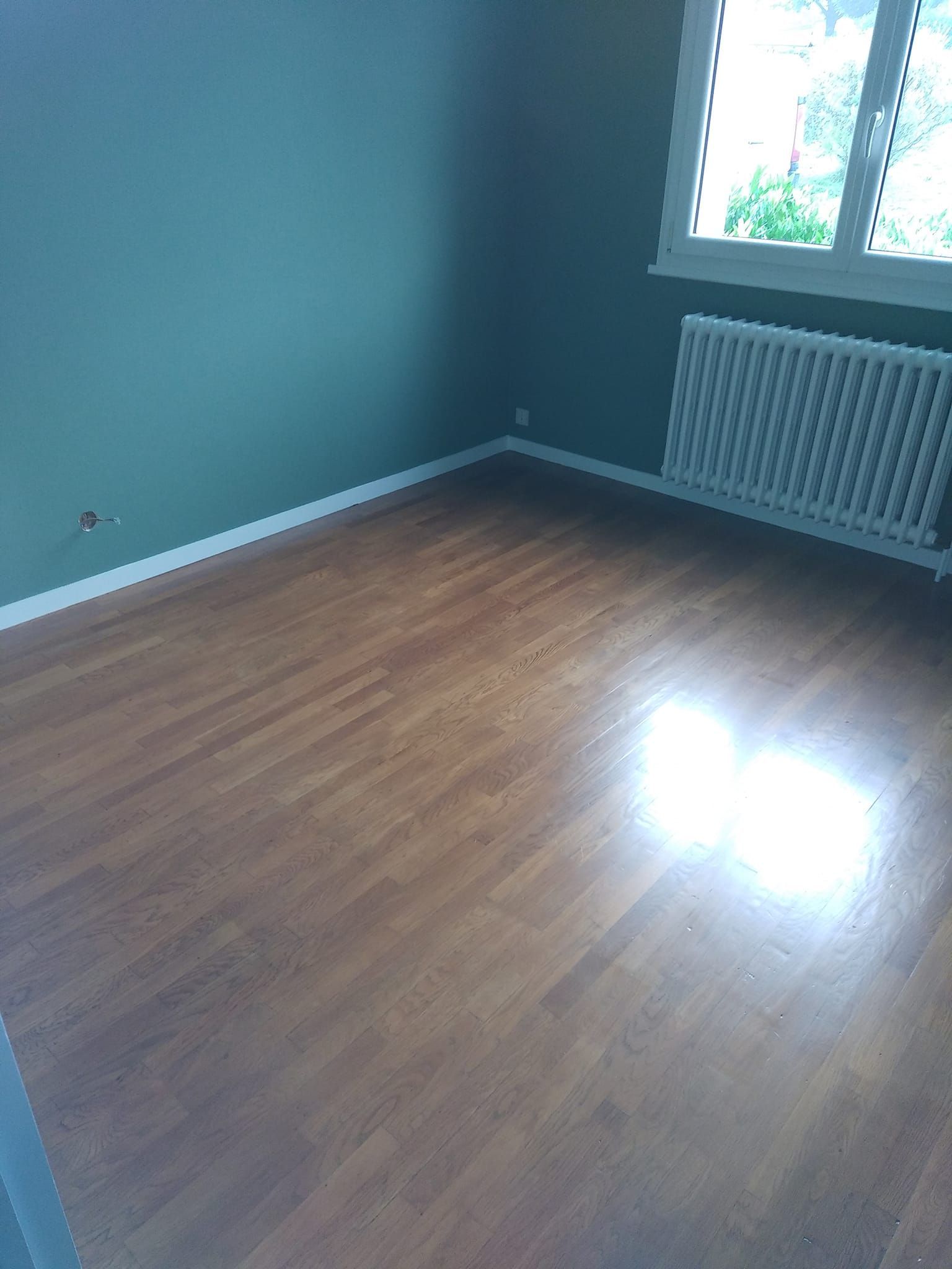 Pièce vide avec parquet et murs bleu sarcelle.