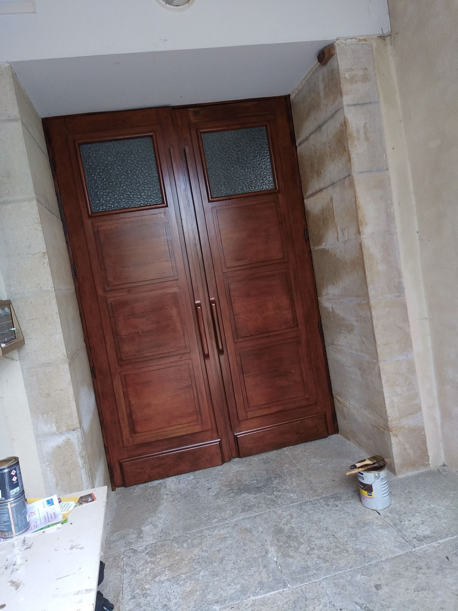 Portes doubles en bois avec panneaux de verre, encastrées dans une porte en pierre.