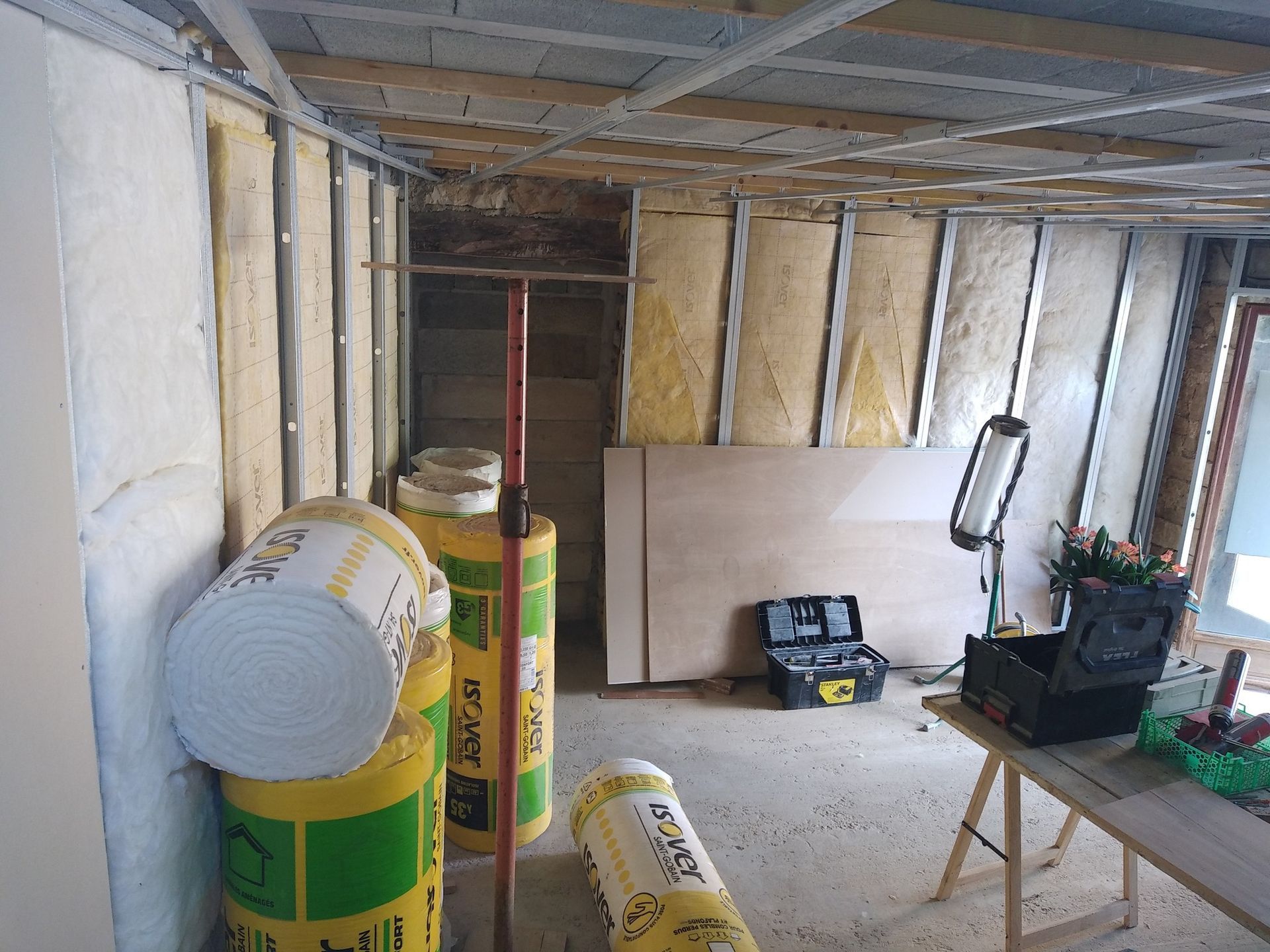Chantier intérieur, rouleaux d'isolant jaune, outils, charpente, feuilles de contreplaqué.
