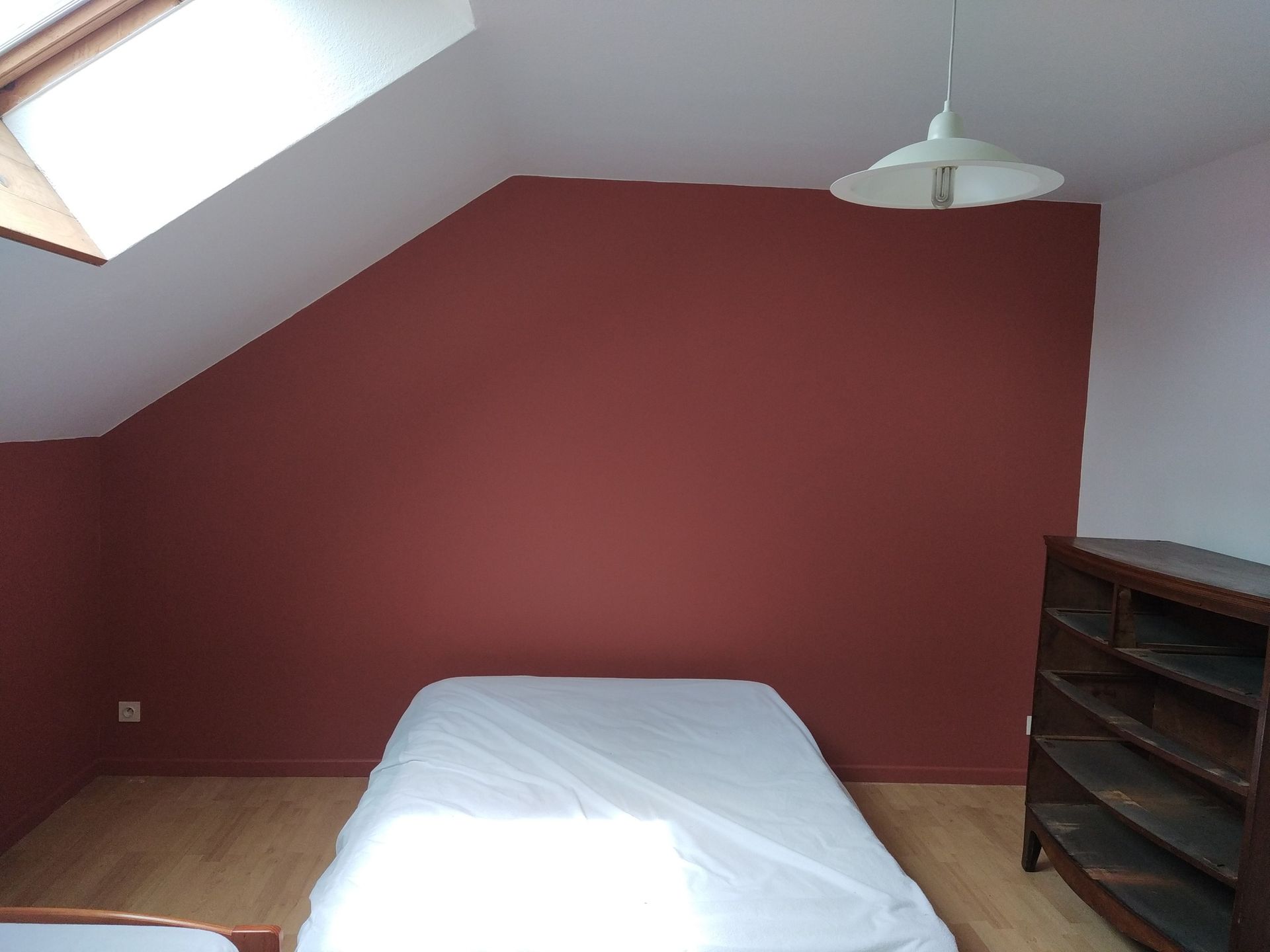 Chambre avec plafond incliné, mur marron, lit, plancher de bois et une commode.