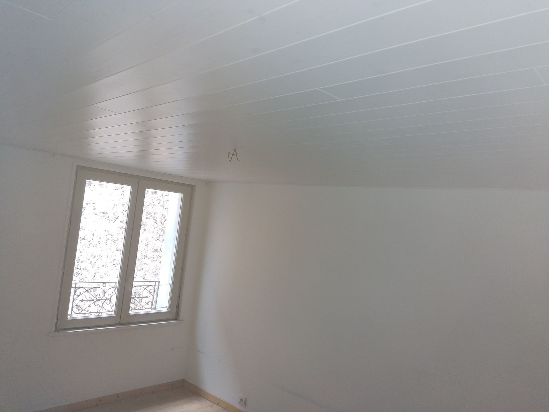 Chambre blanche avec une fenêtre, un plafond blanc et un sol de couleur claire.
