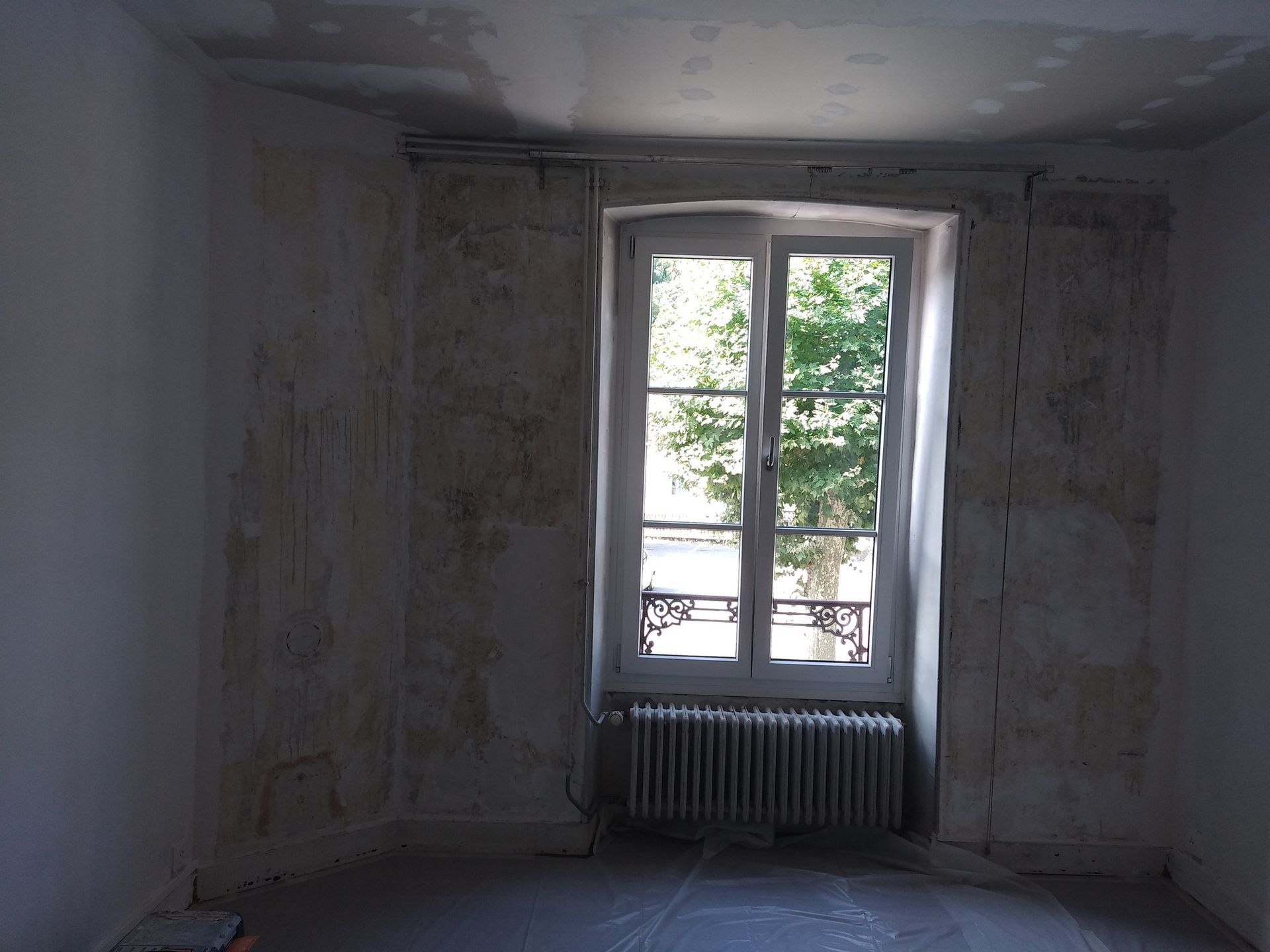 Pièce intérieure nue avec fenêtre et radiateur, murs décapés de plâtre.