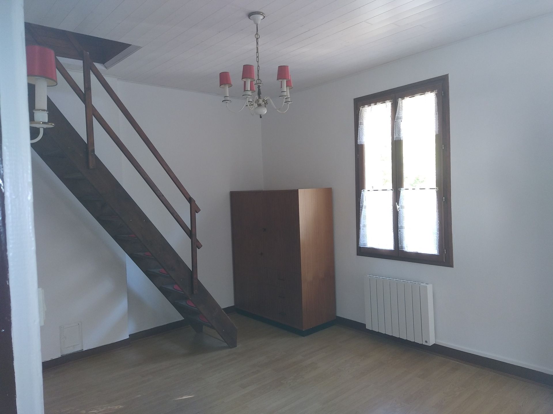 Escalier et armoire en bois dans une pièce avec fenêtre et lustre.