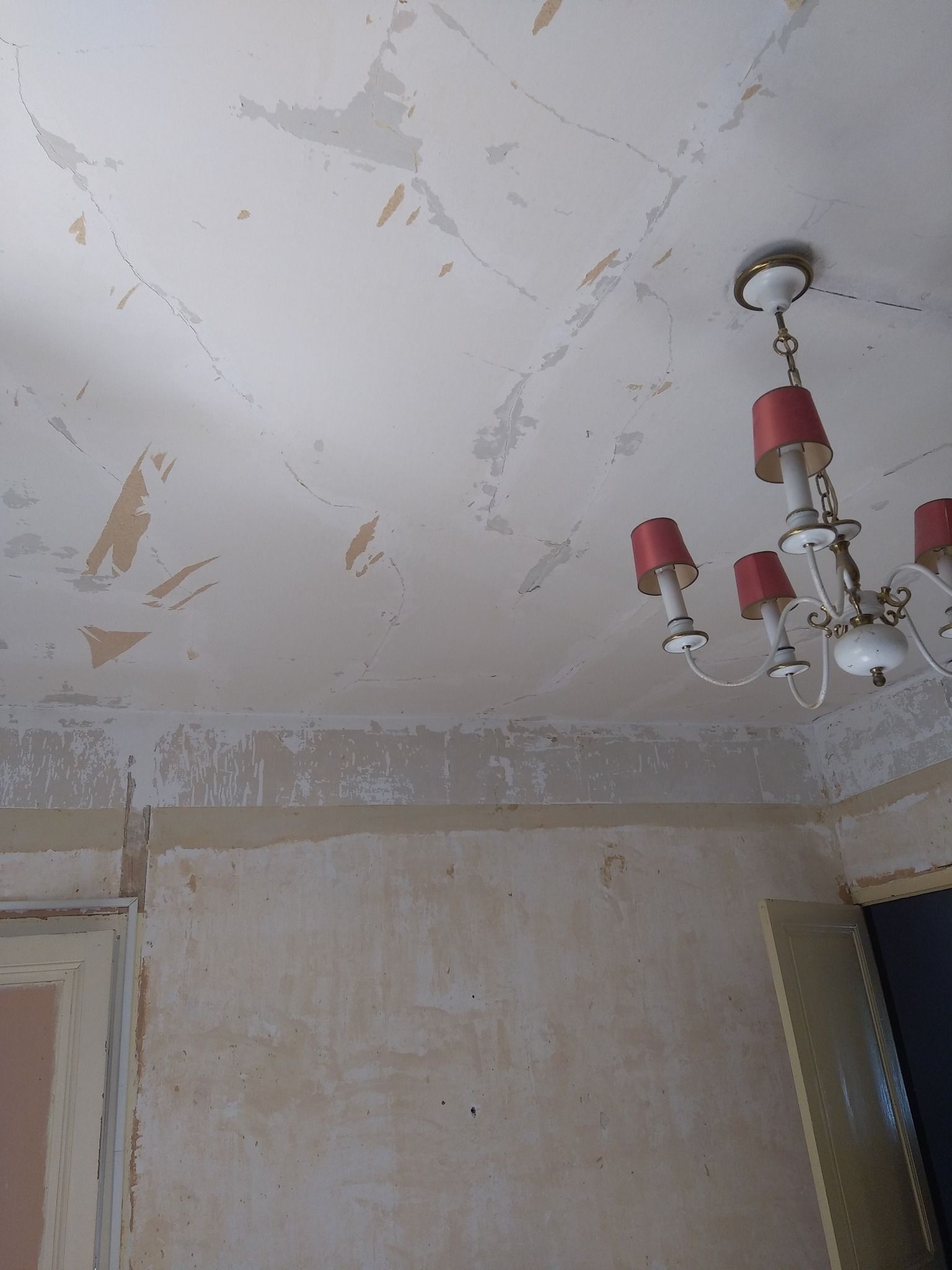 Plafond et mur avec peinture écaillée, un lustre est suspendu au plafond.