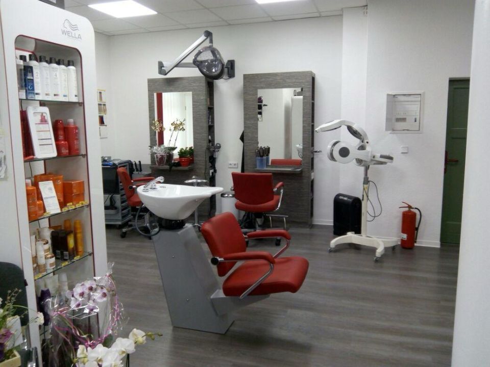 Interieur eines Friseursalons mit Frisierplätzen, roten Stühlen, Spiegeln und Produktregalen.