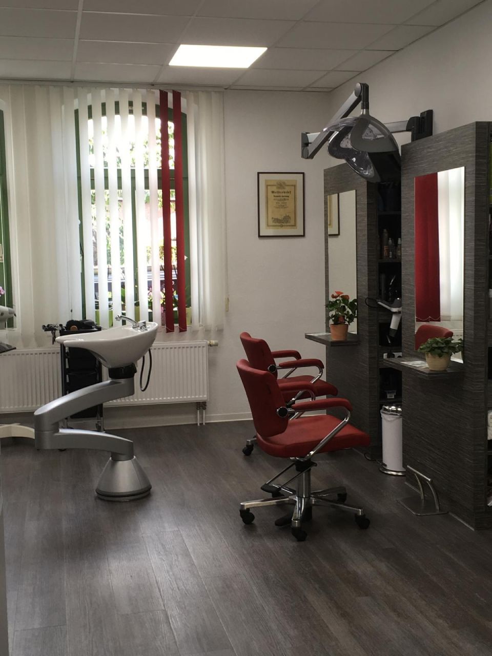 Innenansicht eines Friseursalons mit rotem Friseurstuhl, Waschbecken, Spiegeln und Haartrockner.