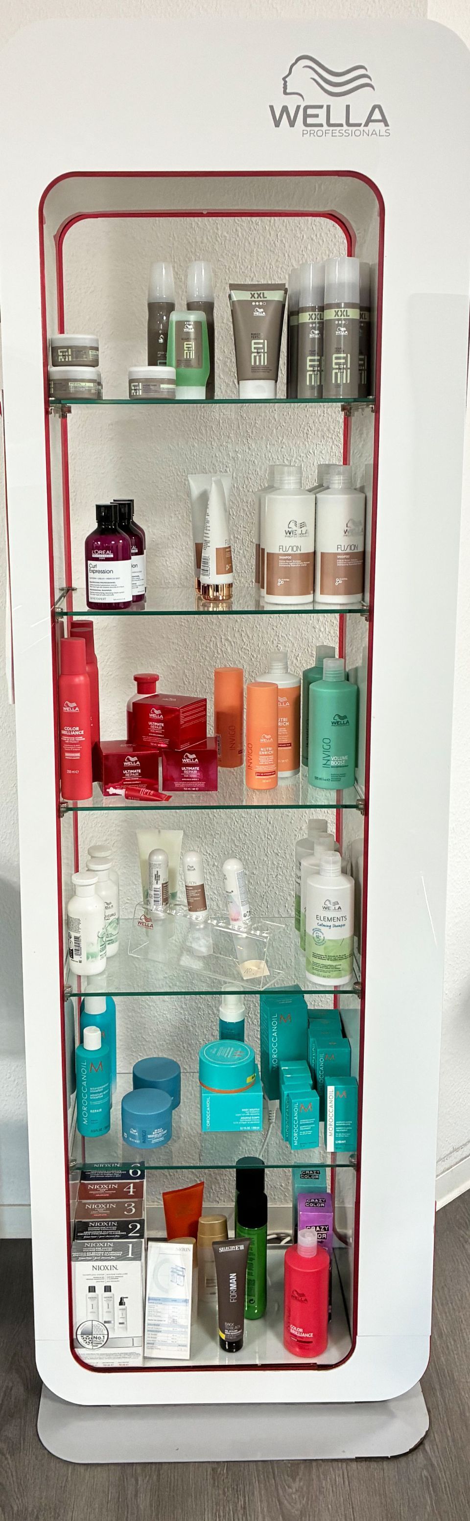 Ein weißer Vitrinenschrank mit Regalen, in denen verschiedene Haarprodukte aufbewahrt werden, darunter Flaschen, Tiegel und Tuben.