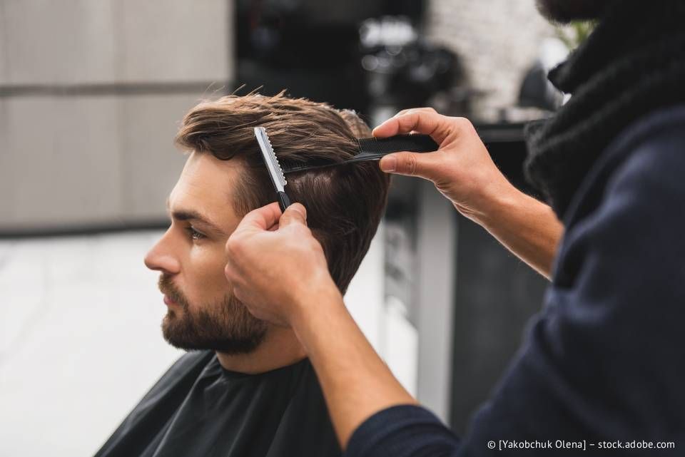 Ein Mann lässt sich im Salon die Haare schneiden. Der Friseur kämmt das braune Haar des Kunden mit einem schwarzen Kamm und einem Rasiermesser.