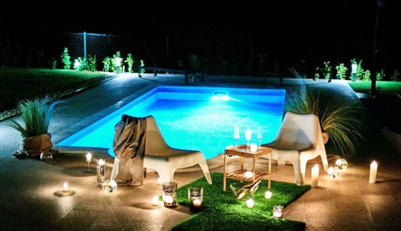 Ein Swimmingpool wird nachts mit Kerzen und Stühlen darum herum beleuchtet.