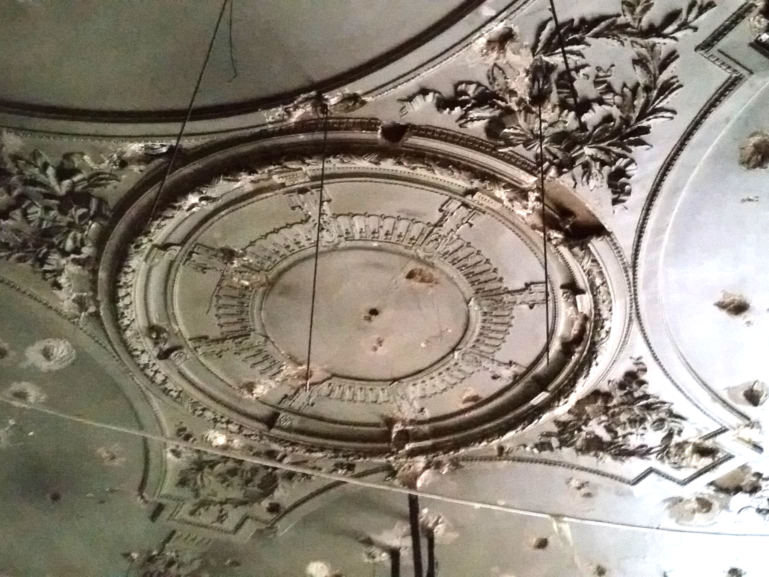 Médaillon circulaire ornemental au plafond d'un dôme présentant des signes de vieillissement et des détails architecturaux.