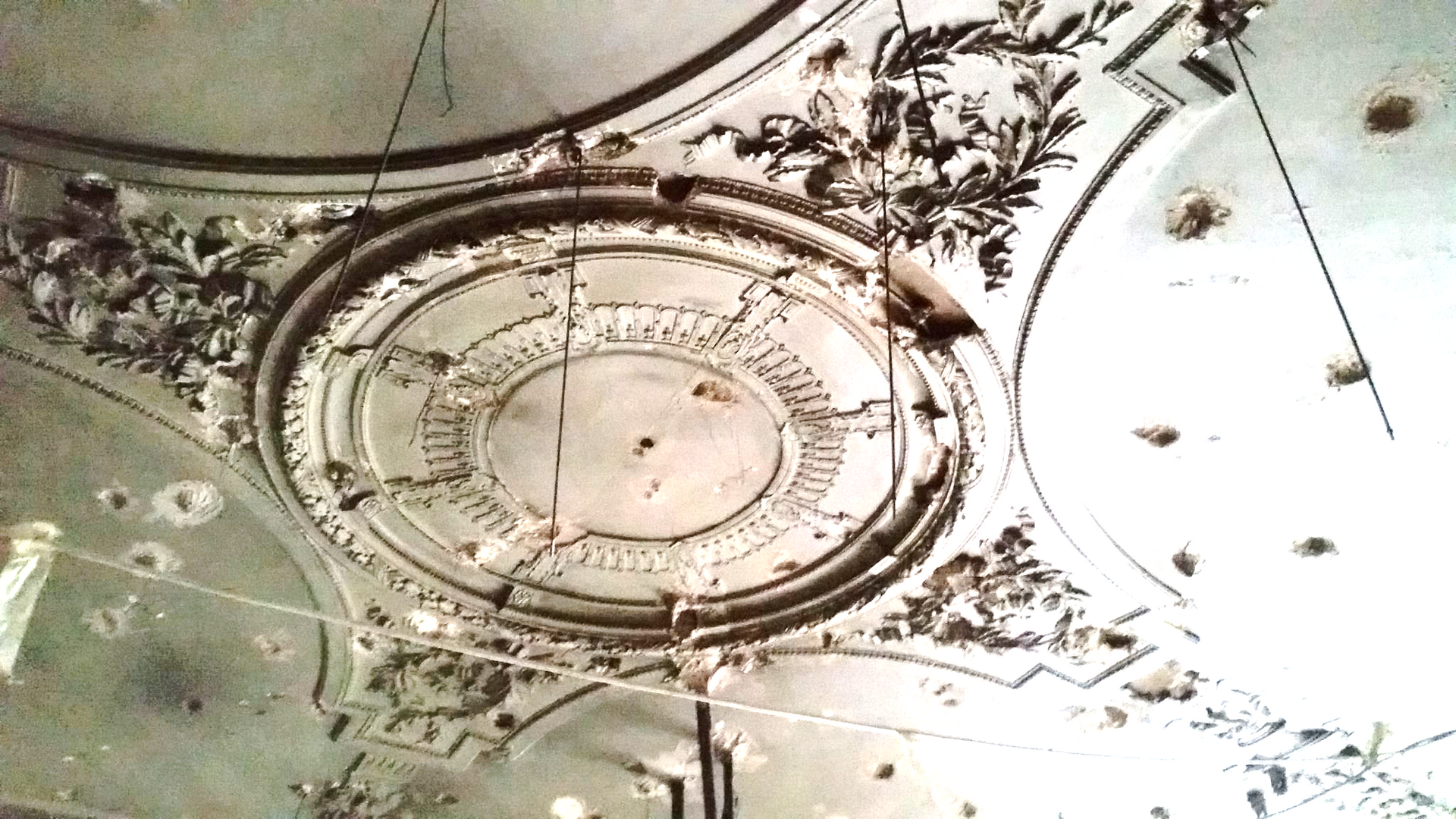 Médaillon de plafond circulaire en plâtre blanc orné de détails en relief, représentant des motifs végétaux et géométriques.